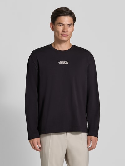 Männermodel trägt schwarzes Regular Fit Longsleeve aus reiner Baumwolle Modell 'Ryan' von Wood Wood, Logo-Stitching, Nahaufnahme Oberkörper.
