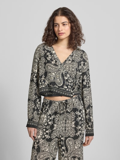 Frauenmodel trägt Shaped Fit Bluse aus reiner Viskose Modell 'LEMZA' von Only mit florales-Allover-Muster, Wickeloptik, Bindegürtel, V-Ausschnitt, Langarm, Manschette, feine Webstruktur, Farbe Schwarz-Creme, Ganzkörperansicht von vorne.