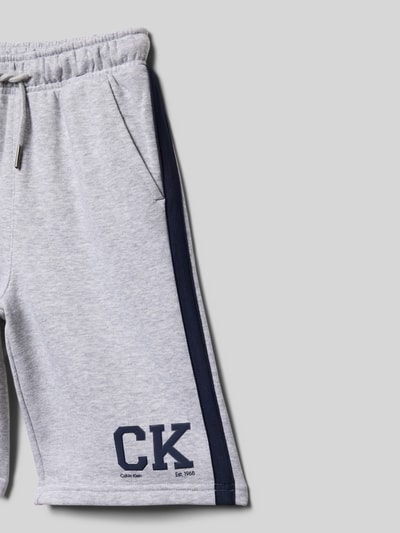 Produktfoto, Relaxed Fit Sweatshorts aus Baumwoll-Mix Modell 'VARSITY' von Calvin Klein Jeans in Hellgrau mit Logo-Applikation, Kontraststreifen und elastischem Bund, Sweat-Material, seitliche Eingrifftaschen