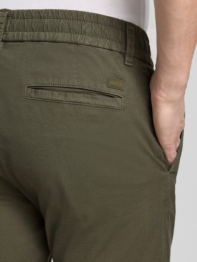 Mężczyzna nosi Tapered Chino aus Baumwoll-Mix Modell 'CHINO-TAPERED-DS-10' od BOSS Orange, kolor jednolity, bawełniany materiał, tylne kieszenie, elastyczny pas, detal z logo, krój tapered fit, zdjęcie detaliczne tylnej części.