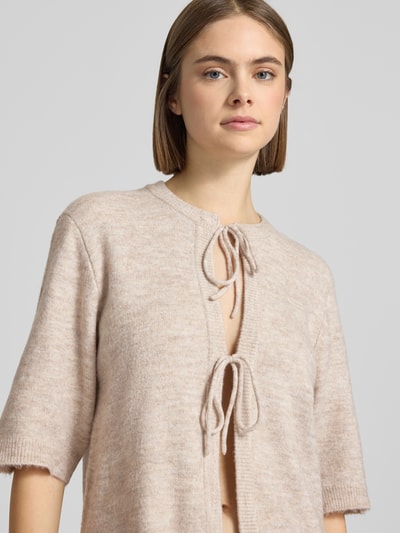 Frauenmodel trägt Regular Fit Cardigan mit Schnürungen Modell 'SIMONI' von Only in beige, Strickoptik, unifarben, Nahaufnahme Oberkörper.