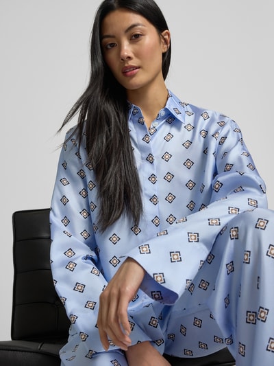 Vrouwenmodel draagt Relaxed Fit Hemdbluse uit zuivere zijde Model 'DISCO' van MM by Max Mara in lichtblauw met grafisch patroon, satijn, doorknoopsluiting, overhemdkraag, geheel beeld van voren.
