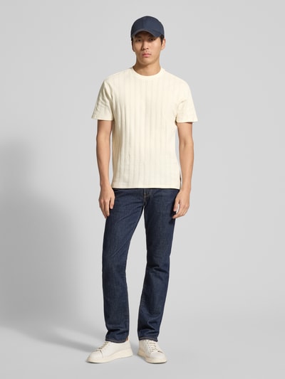Męski model nosi Regular Fit T-Shirt aus Baumwolle od Guess, bawełna, krój regular fit, okrągły dekolt, detal z logo, długość tyłu 69 cm w rozmiarze M, całopostaciowy widok z przodu.