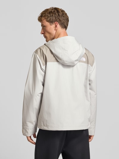 Męski model prezentuje kurtkę z kapturem z wyhaftowanym logo Jacke mit Label-Stitching Modell 'REIGN ON 2.0' von The North Face, krój regular fit, kolor jasnoszary z beżowym, długość tyłu w rozmiarze M 69 cm, szerokość ramion w rozmiarze M 52 cm, szerokość klatki piersiowej w rozmiarze M 63 cm, długość rękawów w rozmiarze M 65 cm, widok całej sylwetki z tyłu.