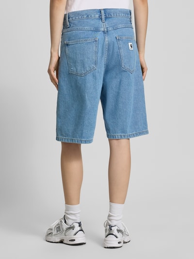 Frauenmodel trägt Relaxed Fit Jeans Shorts aus reiner Baumwolle Modell 'Brandon' von Carhartt Work In Progress, 5-Pocket-Design, Label-Patch, hellblaue Jeans-Optik, Ganzkörperansicht Rückansicht.