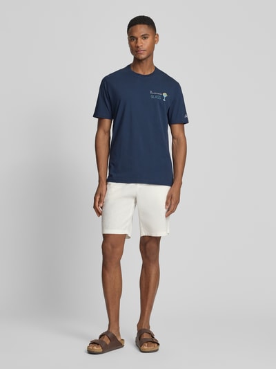 Męski model nosi t-shirt z haftami model 'PORTOFINO' od MC2 Saint Barth, bawełna, krój regular fit, okrągły dekolt, długość tyłu 68 cm, granatowy, prosta faktura, widok całej sylwetki z przodu.