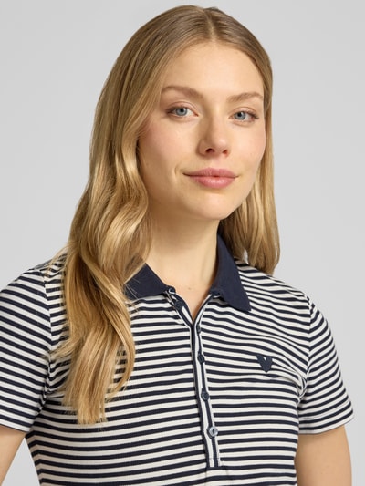 Modelka kobieca nosi Regular Fit Poloshirt aus Baumwoll-Mix od Tom Tailor, efekt: wzór w paski, wyhaftowany motyw, kołnierzyk polo, dekolt w serek, listwa guzikowa, rękaw: krótki, wykończenie materiału: pika, materiał: mieszanka bawełny, zbliżenie na górną część ciała