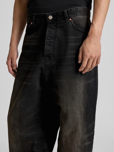 Männermodel trägt schwarze Jeans mit leichter Used-Waschung, silbernem Knopf und Eingrifftaschen, Nahaufnahme Oberkörper.