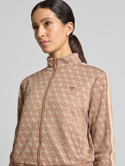 Frauenmodel trägt Regular Fit Sweatjacke mit Allover-Logo-Print von GUESS aus elastischem Material-Mix in Beige und Weiß, Nahaufnahme Oberkörper.