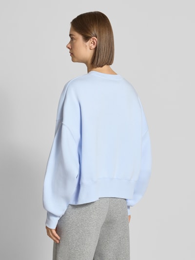 Frauenmodel trägt Relaxed Fit Sweatshirt aus reiner Baumwolle Modell 'Phoenix' von Nike in Hellblau, kombiniert mit grauer Hose, Damen Sweatshirt von Nike, Ganzkörperansicht Rückansicht.