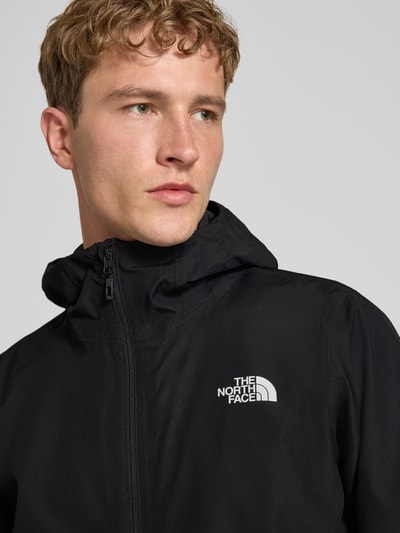 Männermodel trägt Regular Fit Jacke mit Logo-Print Modell 'Quest' von The North Face in Schwarz mit Kapuze, Nahaufnahme Oberkörper, Damenjacke.