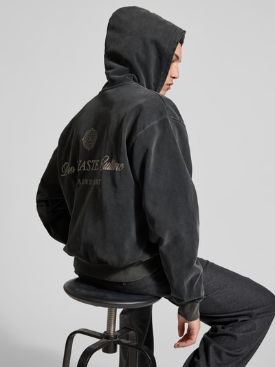 Männermodel trägt Oversized Jeansjacke aus Baumwoll-Mix von Don't Waste Culture, dunkle Farbe, elastische Abschlüsse, Rückenlänge 65 cm, Ganzkörperansicht Rückansicht.