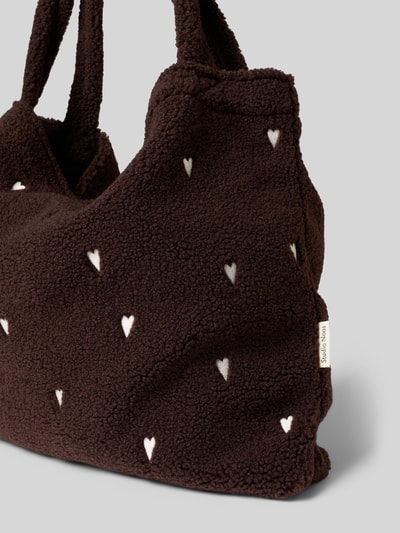 Produktfoto, Tote Bag aus Teddyfell von Studio Noos, dunkelbraun mit Allover-Stitching in Herzform, sichtbares Stoffschild, strukturierte Textur, offenes Hauptfach und Schulterriemen, Maße ca. 60x40x10 cm, Länge Schulterriemen ca. 72 cm.