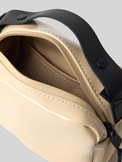 Produktfoto, cremefarbene Handtasche mit Reißverschluss Modell 'BOX BAG MICRO' von RAINS, glatte Textur, Label-Detail erkennbar, Hauptfach mit Meshfutter, verstellbarer schwarzer Schulterriemen, Maße 17x12x8 cm, Riemenlänge 87 cm