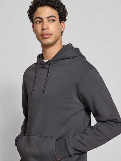 Mannenmodel draagt Regular Fit Hoodie aus Baumwoll-Mix Modell 'CERES' van Only & Sons in effen donkergrijs, sweatmateriaal, label stitching, kangoeroezak, geribde boorden, kap met trekkoord. Nahaufnahme Oberkörper.