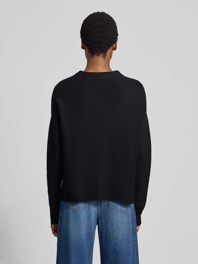 Frauenmodel trägt schwarzen Loose Fit Pullover aus reiner Baumwolle Modell 'MERINAA' von ARMEDANGELS, glatte Textur, Ganzkörperansicht Rückansicht.