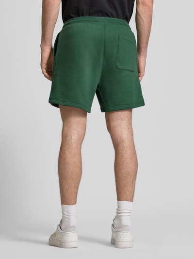 Mężczyzna model nosi Szorty Regular Fit aus Baumwoll-Mix von Tommy Jeans, efekt: jednolity kolor, detal z logo, tunel, elastyczny ściągacz, kieszeń z tyłu, wpuszczane kieszenie, dzianina dresowa, mieszanka bawełny, widok całej sylwetki od tyłu.