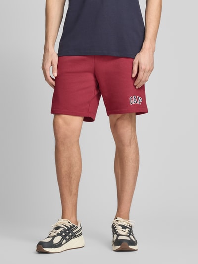 Männermodel trägt Sweatshorts mit Logo und elastischem Bund von GAP aus Baumwoll-Mix in Rot mit Eingrifftaschen, Regular-Fit, Nahaufnahme Unterkörper.