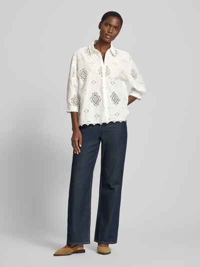 Frauenmodel trägt Regular Fit Bluse mit Häkelspitze Modell 'MURIEL' von Bash, Hemdblusenkragen, verdeckte Knopfleiste, 3/4-Arm, Rückenlänge 65 cm, Ärmellänge 40 cm, weiß mit feinen Cut-Outs und geometrischem Muster auf glatter Oberfläche, kombiniert mit dunkler Jeans, Ganzkörperansicht von vorne.