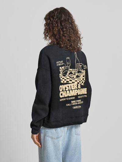 Modelka nosi Regular Fit Sweatshirt mit Logo-Print od ANOTHER COTTON LAB, mieszanka bawełny, stójka, elastyczne wykończenia, nadruk z logo, widok całej sylwetki z tyłu.