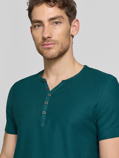 Männermodel trägt T-shirt mit V-hals en knoopsluiting van MCNEAL in regular fit van puur katoen in donkere groentint, nahaufnahme oberkörper. Ruglengte bij maat M: 68 cm.