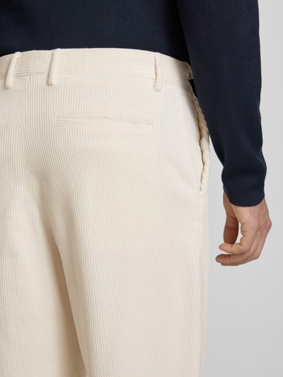 Männermodel trägt High Waist Cordhose mit Bundfalte Luke von Selected, jednokolorowe, kieszenie wpuszczane, zapięcie na guzik i zamek błyskawiczny, szlufki, zakładka w pasie, tylna kieszeń, widoczna tekstura sztruksu, spodnie sztruksowe, materiał o lekko kremowym odcieniu, Ganzkörperansicht Rückansicht.