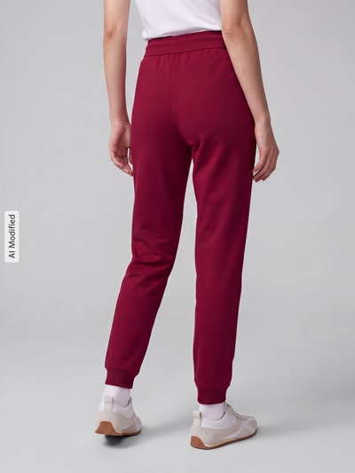 Vrouwenmodel draagt Regular Fit Jogpant uit katoenmix model 'Hugo ID Pant' van HUGO, donkerrode kleur, zachte stof, dames jogpant, volledige achteraanzicht, KI-gemodificeerd beeld