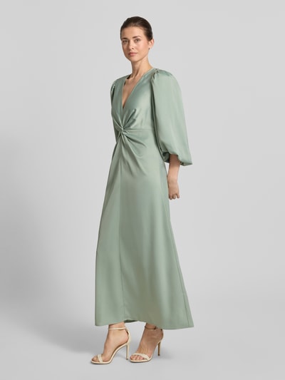 Frauenmodel trägt Damen Maxikleid mit Ballonärmeln, V-Ausschnitt und Knoten-Detail, Modell 'THEA' von YAS, Material-Mix mit Stretch-Anteil, taillierter Schnitt; zartgrüne, glatte Textur, Ganzkörperansicht von vorne.