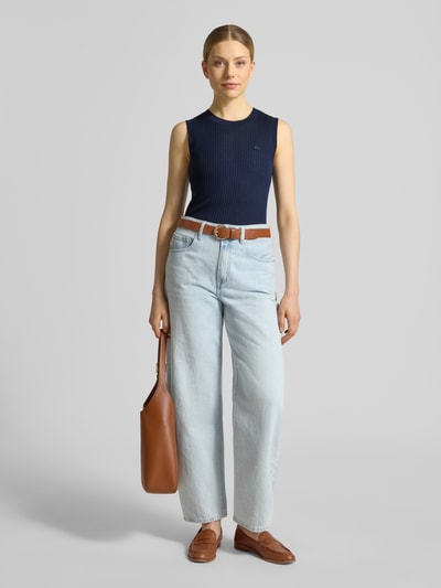 Frauenmodel trägt Slim Fit Pullunder aus reiner Wolle von Lacoste in Strickoptik mit Rundhals, gestreifte Struktur, Logo-Detail, Rippstrick, Ganzkörperansicht von vorne.