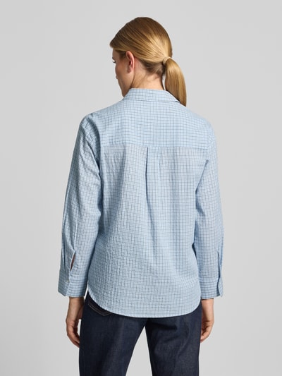 Frauenmodel trägt Relaxed Fit Hemdbluse aus reiner Baumwolle Modell 'CHUACKUA' von MANGO in hellblau kariert, verlängerte Rückseite, Ganzkörperansicht Rückansicht.