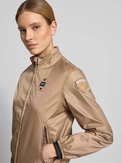 Vrouwenmodel draagt Jacke mit Zweiwege-Reißverschluss Modell 'ANNABEL' van Blauer Usa in regular fit, lichte bruintint, staande kraag, labeldetails, ritszakken, detailopname bovenlichaam.