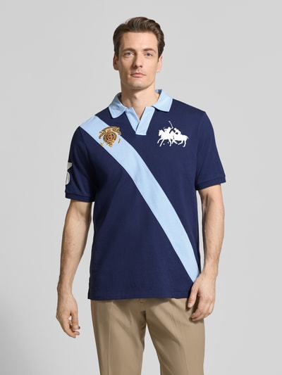 Männermodel trägt Regular Fit Poloshirt aus reiner Baumwolle von Polo Ralph Lauren, navy mit hellblauem Streifen, Logo-Stitching, Two Tone, Kontraststreifen, Polokragen, Kurzarm, Ganzkörperansicht von vorne.
