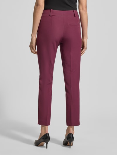 Frauenmodel trägt Regular Fit Schmale Hose mit Bügelfalten Modell 'Hedima-1' von HUGO in unifarben Beere, Logo-Detail, Ganzkörperansicht Rückansicht.
