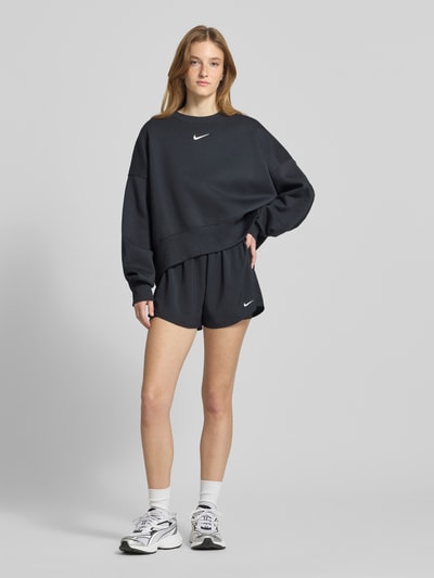 Frauenmodel trägt Sweatshirt mit Logo Modell 'Phoenix' von Nike im Regular Fit aus Baumwoll-Elasthan-Mix, dunkle Farbe, Ganzkörperansicht von vorne.