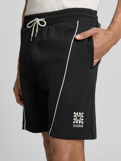 Männermodel trägt Regular Fit Sweatshorts aus Baumwoll-Mix Modell 'DARYNTO' von HUGO, Optik: Unifarben, Logo-Stitching, Kontraststreifen, Bundabschluss: elastisch mit Tunnelzug, seitliche Eingrifftaschen, Materialverarbeitung: Sweat, Nahaufnahme Oberschenkel.