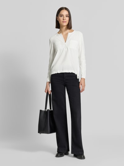 Frauenmodel trägt Regular Fit Bluse mit Brusttaschen von monari in Weiß, Ziersteinbesatz, Tunika-Ausschnitt, locker fallender Stoff, Ganzkörperansicht von vorne.