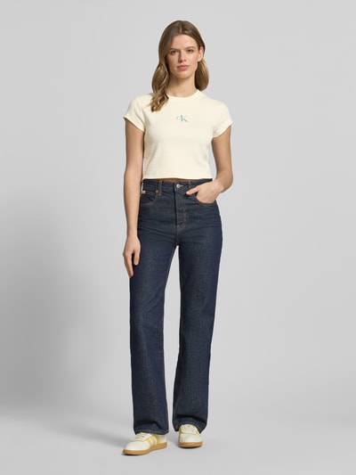 Modelka nosi Cropped T-Shirt mit Streifenmuster und Logo od Calvin Klein Jeans, kremowe paski, logo na piersi, bawełna z elastanem, okrągły dekolt, długość tyłu S: 39 cm, widok całej sylwetki z przodu