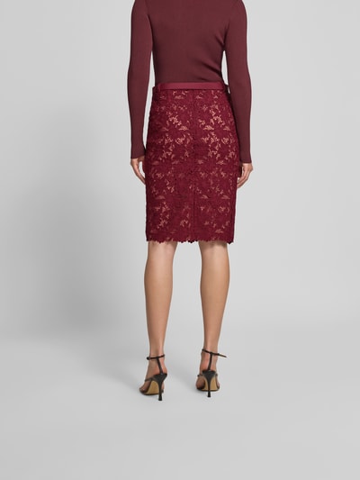 Frauenmodel trägt Slim Fit Rock mit Allover-Spitzenbesatz von Self-Portrait in Bordeaux, Knielänge, mit abnehmbarem Gürtel, Blickdichter Unterrock, Gesamtlänge 64 cm, Bundweite 38 cm, Ganzkörperansicht Rückansicht.