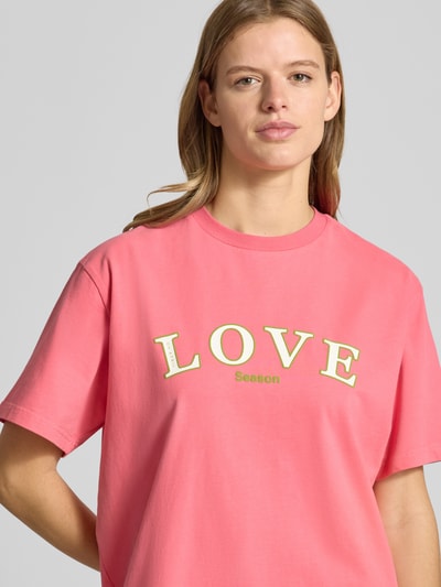 Frauenmodel trägt T-Shirt mit Statement-Print und Rundhalsausschnitt von OH APRIL in Pink, Oversized aus reiner Baumwolle, Nahaufnahme Oberkörper.
