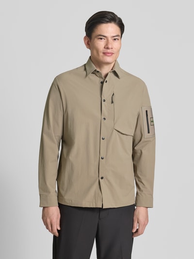 Męski model nosi Relaxed Fit Overshirt mit Label Patch Modell 'ST_GLOBE HEXA L' von BOSS Green, efekt: jednolity kolor, krój relaxed fit, wykładany kołnierz, listwa z zatrzaskami, aplikacja z metką, długi rękaw, hydrofobowy, wpuszczane kieszenie, brustasza, ganzkörperansicht von vorne.