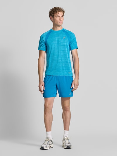 Męski model nosi Regular Fit T-Shirt mit Logo-Print Modell 'Road' von ASICS TIGER w kolorze niebieskim, półprzejrzysty materiał, okrągły dekolt, Długość tyłu w rozmiarze M: 69 cm, Ganzkörperansicht von vorne