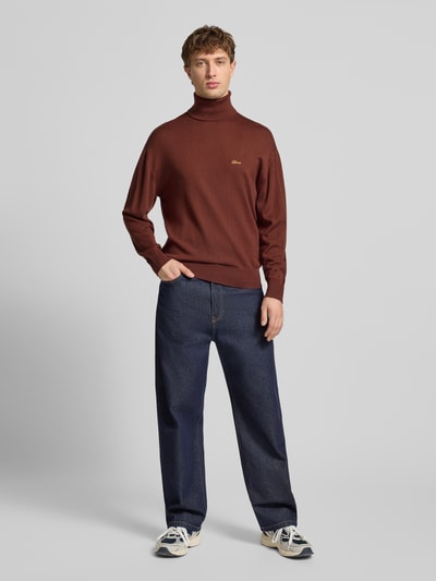 Männermodel trägt Loose Fit Rollkragenpullover aus Woll-Mix von BLKVIS in Braun mit gerippten Abschlüssen und Label-Stitching, Ganzkörperansicht von vorne.