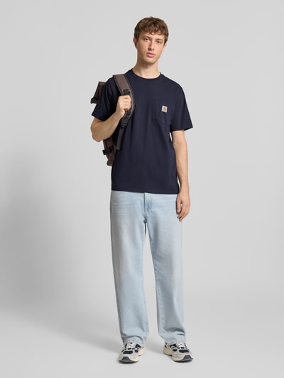 Męski model nosi Regular Fit T-Shirt mit Logo-Patch od Carhartt Work In Progress, bawełna, kieszeń na piersi, dekolt okrągły, krój regular fit, długość tyłu w rozmiarze M: 70 cm, widok całej sylwetki z przodu.