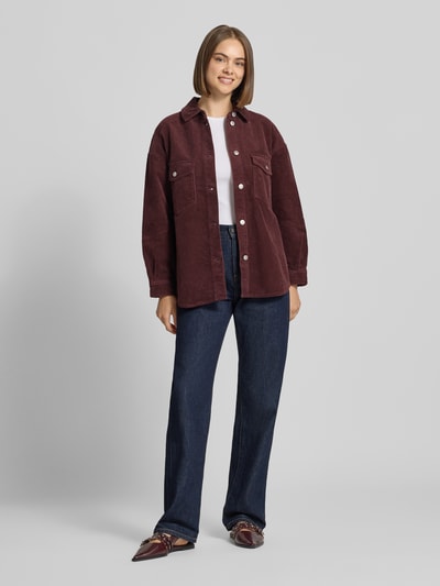 Frauenmodel trägt Loose Fit Hemdjacke aus reiner Baumwolle Modell 'TIGGY' von ONLY in Dunkelrot, Cord, Ganzkörperansicht von vorne. Unifarben, Umlegekragen, einreihige Knopfleiste, Longline Länge, langarm mit Manschette, abgerundeter Rumpfabschluss, Brusttaschen, Cordstruktur, Damen Hemdjacke.