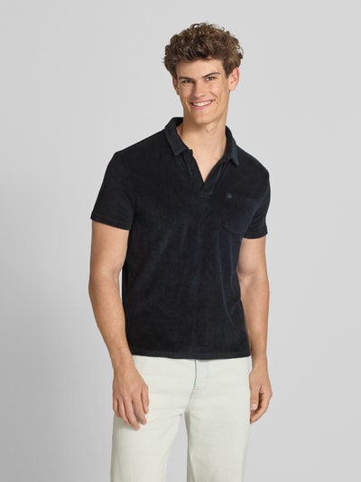 Männermodel trägt schwarzes Slim Fit Poloshirt aus Frottee von Superdry, reine Baumwolle, offener Kragen, kurzärmelig, Ganzkörperansicht von vorne.