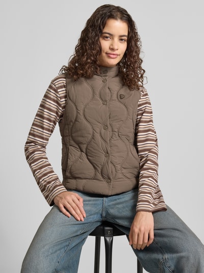 Frauenmodel trägt Steppweste mit Stehkragen und Label-Stitching von Superdry in Braun, Slim Fit, Knopfleiste, Eingrifftaschen, Ganzkörperansicht von vorne.