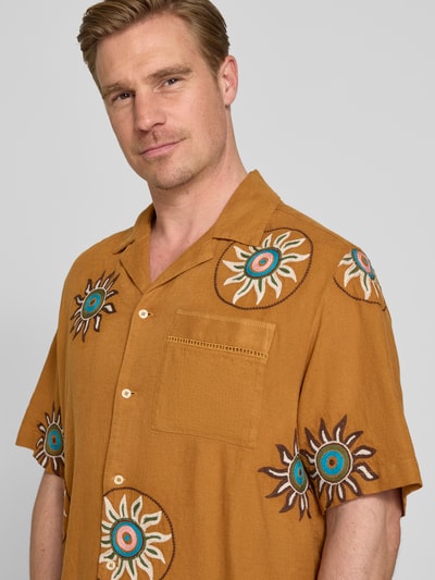 Männermodel trägt Relaxed Fit Freizeithemd aus Leinen-Viskose-Mix mit Brusttasche von Scotch & Soda, florales Allover-Stitching, Kurzärmelig, Reverskragen, Knopfleiste, Nahaufnahme Oberkörper.