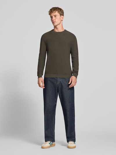 Männermodel trägt Regular Fit Pullover aus reiner Baumwolle Modell 'TONY' von ONLY & SONS in Dunkelgrün, glatte Struktur, Ganzkörperansicht von vorne.