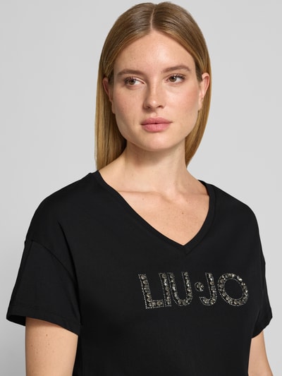 Frauenmodel trägt Regular Fit T-Shirt aus reiner Baumwolle von Liu Jo White in Schwarz mit Ziersteinbesatz und Logo-Detail, Nahaufnahme Oberkörper.