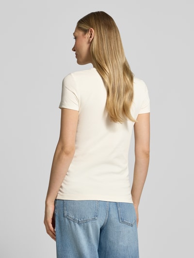 Frauenmodel trägt Slim Fit T-Shirt mit Strasssteinbesatz von Guess in Creme mit Rundhalsausschnitt und Logo-Detail, Rückenlänge 59 cm, Ganzkörperansicht Rückansicht.